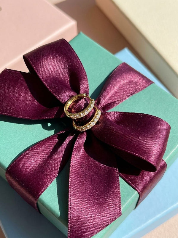 Lundholm Delia kleine oorringen met zirkonia goudkleurig op een groen cadeaudoosje met pruimkleurige satijnen strik