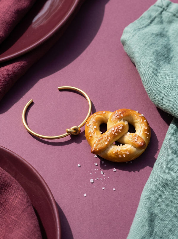 Goudkleurige open bangle naast een brezel