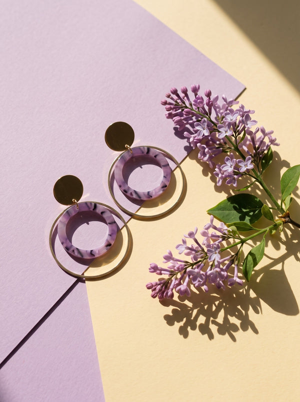 Lundholm Lucienne statement oorhangers met lila ring goudkleurig tussen paarse seringen