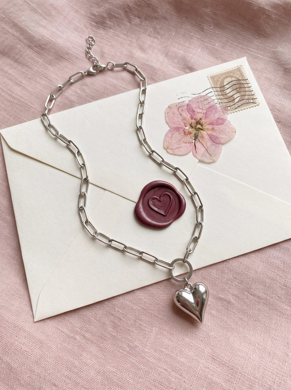 Zilverkleurige hartjesketting op een liefdesbrief met lakzegel