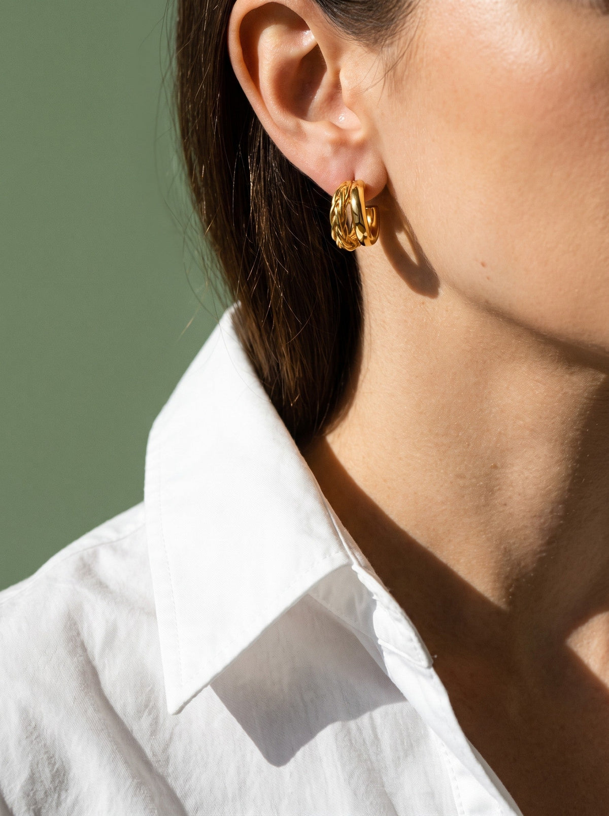 Vrouw in een wit overhemd draagt de Lundholm Fena geometrische hoops goudkleurig, tegen saliegroen