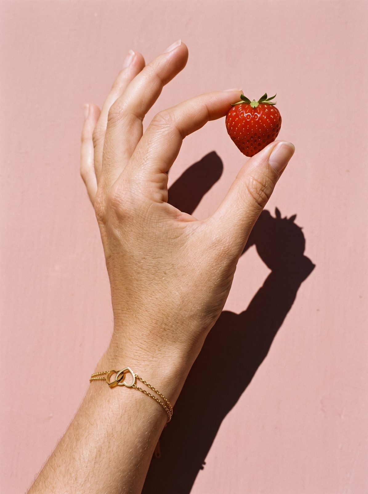 Hand met Lundholm Evie armband met verbonden hartjes houdt een aardbei vast