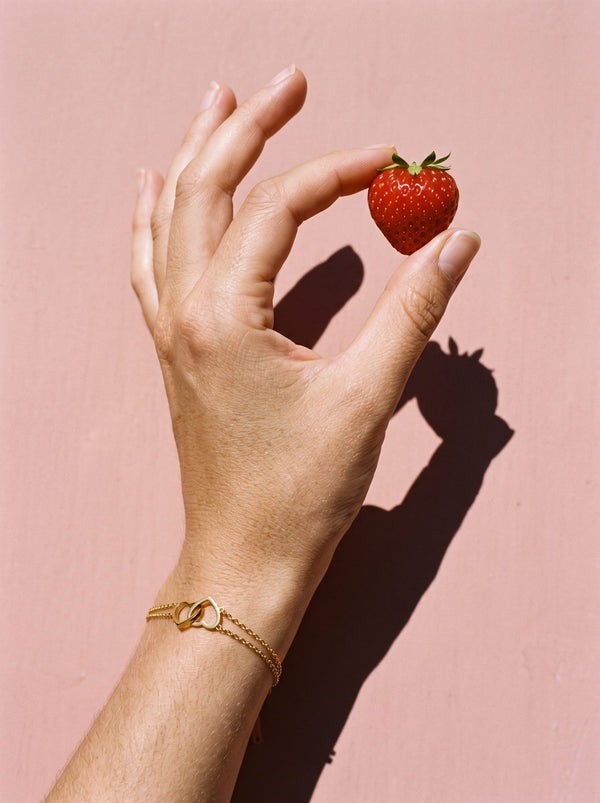Hand met Lundholm Evie armband met verbonden hartjes houdt een aardbei vast