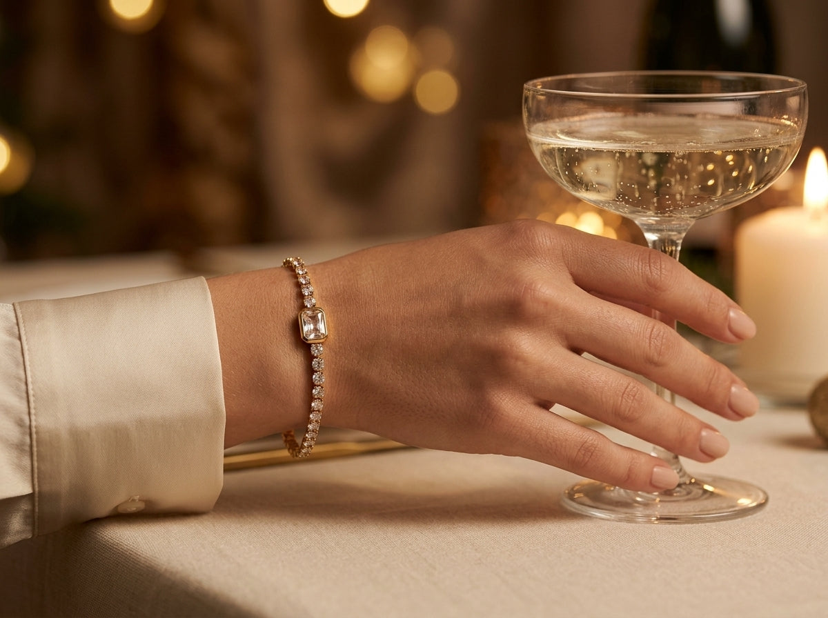 Hand met de Lundholm Jasmijn tennisarmband en een glas champagne bij kerstlicht