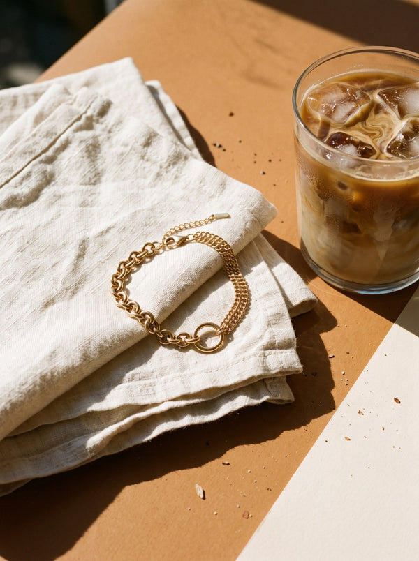Lundholm Madeleine chunky schakelarmband met ring goudkleurig op een linnen servet naast een glas ijskoffie