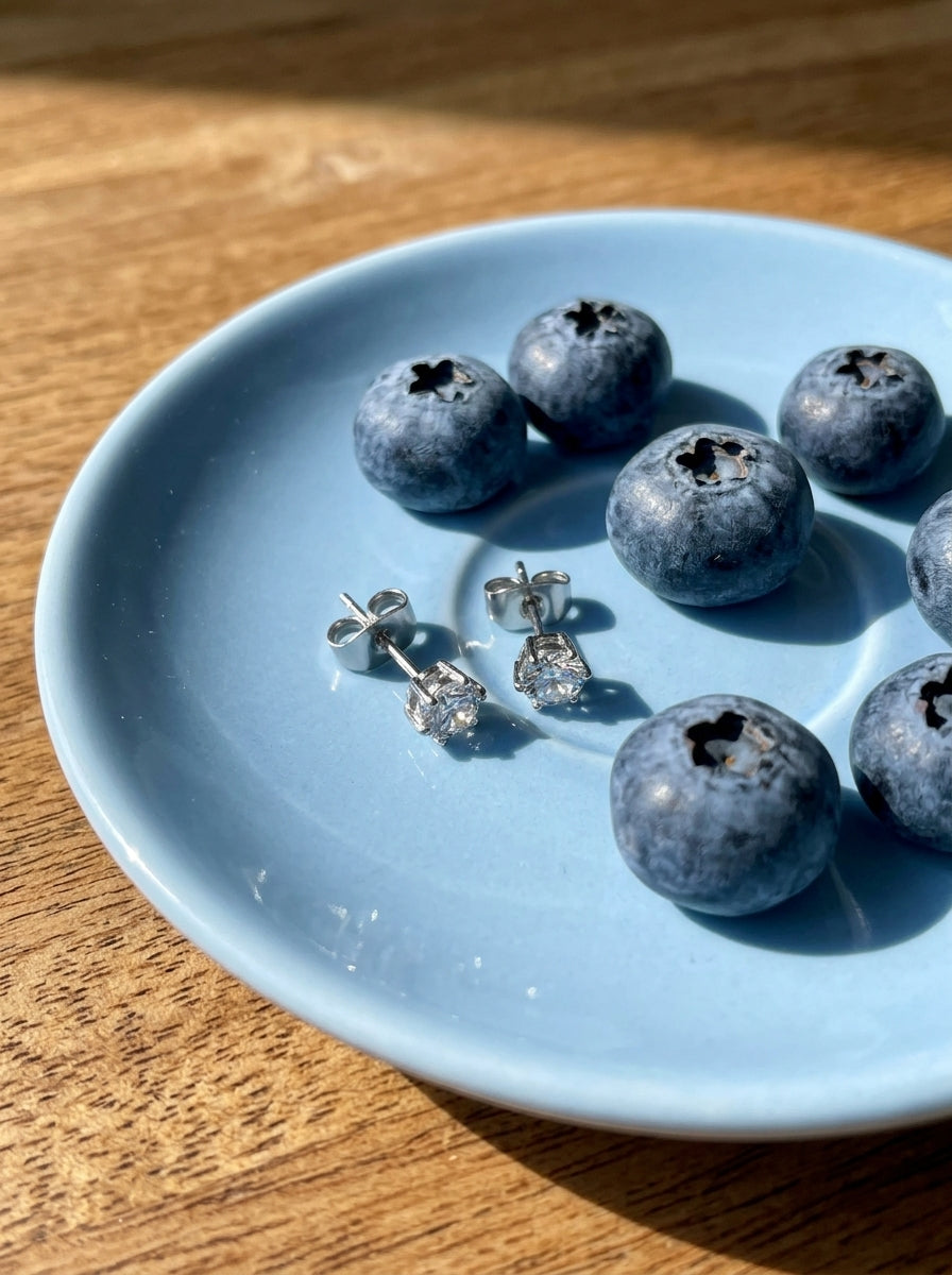 Lundholm Nikki zirkonia oorknopjes 5 mm zilverkleurig op een lichtblauw schoteltje met blauwe bessen op een houten tafel