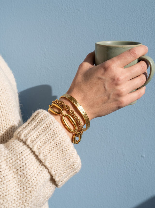 Stapel goudkleurige armbanden en bangles om een pols met een mok