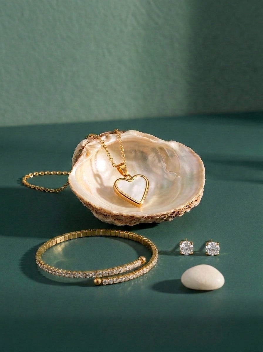 Lundholm Sparkle & Heart look in gold tone: Yael tennis bracelet, Dory heart necklace with mother-of-pearl in a shell and Nikki zirconia studs against sea green