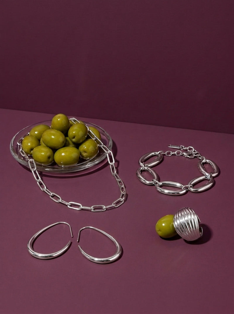 Lundholm look Djärv in zilverkleurig: Elva paperclip ketting, Leanne geometrische oorbellen, Delphine grove schakelarmband en Vanja chunky dome ring bij groene olijven tegen pruimkleur