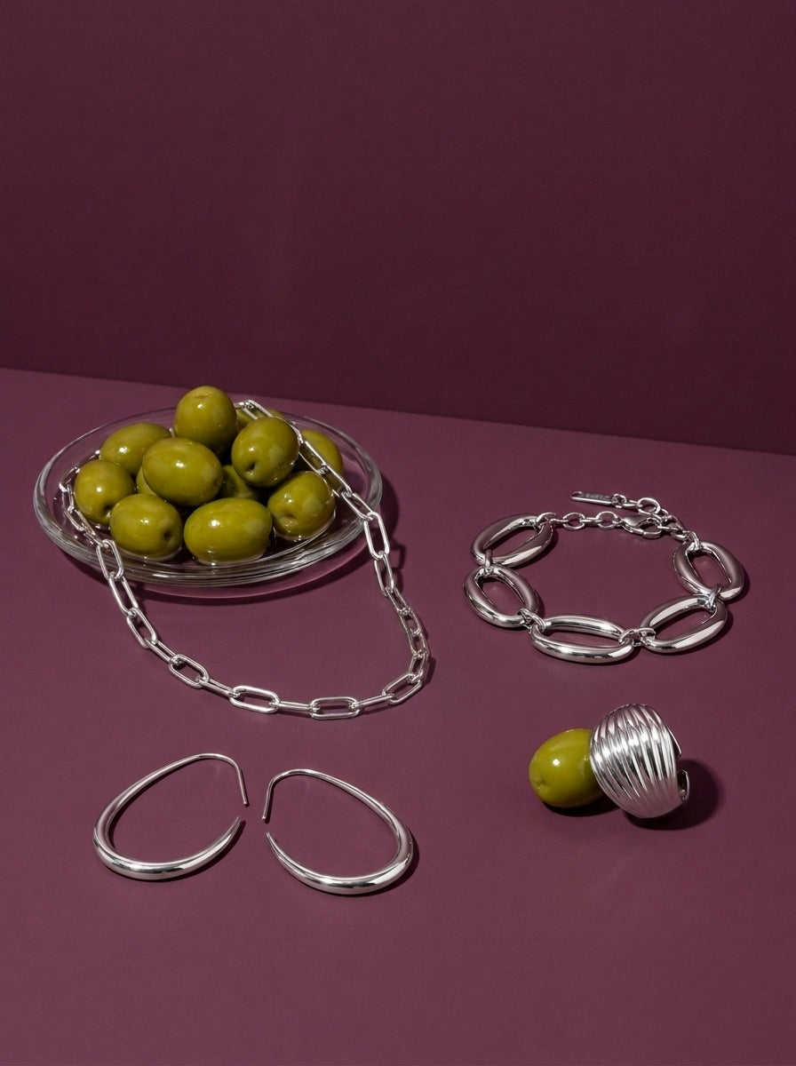 Lundholm Djärv look in silver tone: Elva paperclip necklace, Leanne geometric earrings, Delphine chunky link bracelet and Vanja chunky dome ring by green olives against plum