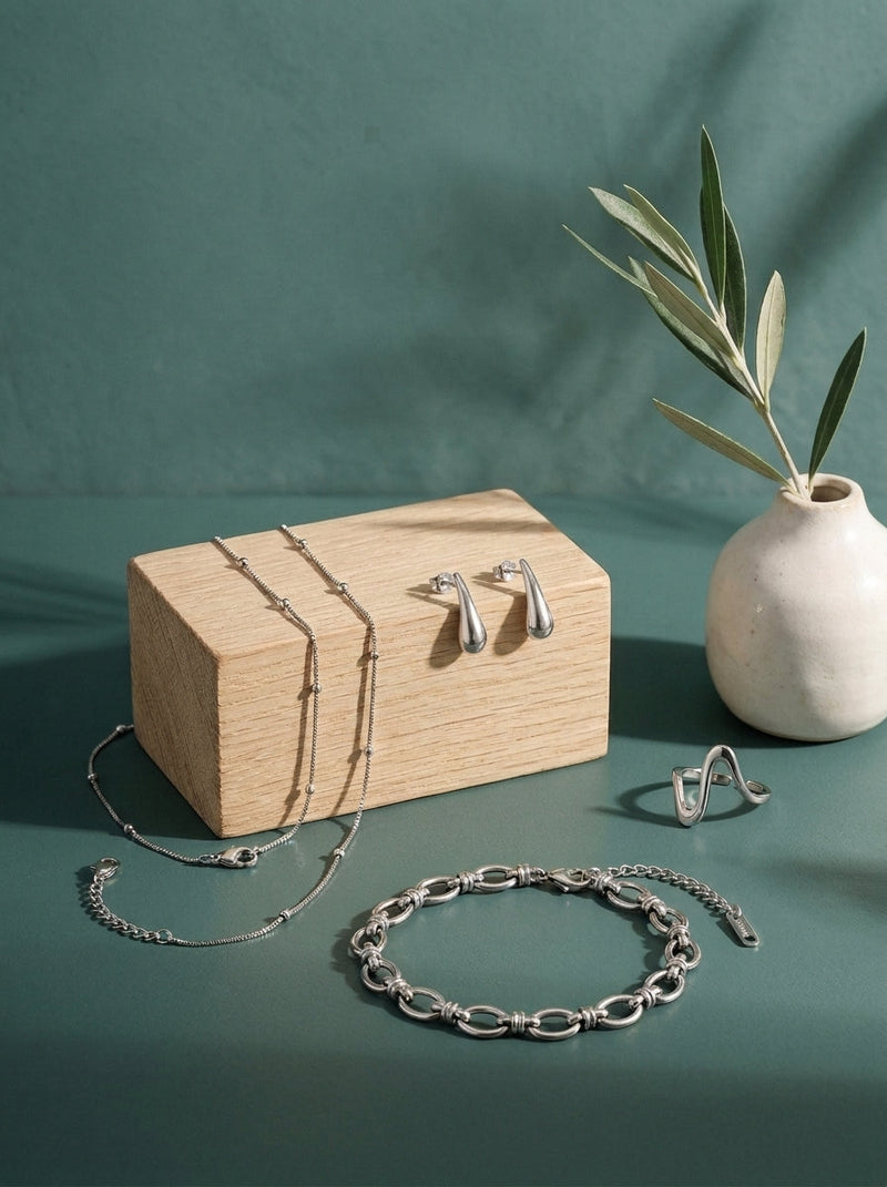 Lundholm look Lagom in zilverkleurig: Mette ketting, Mirthe druppel oorbellen, Ellen armband en Elia ring op eikenhout tegen zeegroen