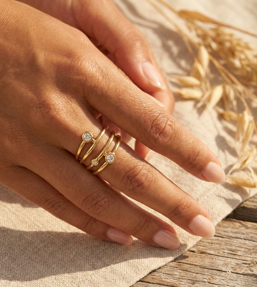Lundholm Alexia goudkleurige verstelbare spiraal ring voor dames met drie fonkelende zirkonia steentjes, gedragen door vrouw met hand op linnen en tarwe halmen voor warme zomerse lookbook lifestyle shoot. Premium stainless steel met PVD gold plating van 2.5 micron, waterproof en hypoallergeen. Een verfijnd cadeau voor vrouw, moeder of vriendin op Moederdag of verjaardag in Scandinavisch design.