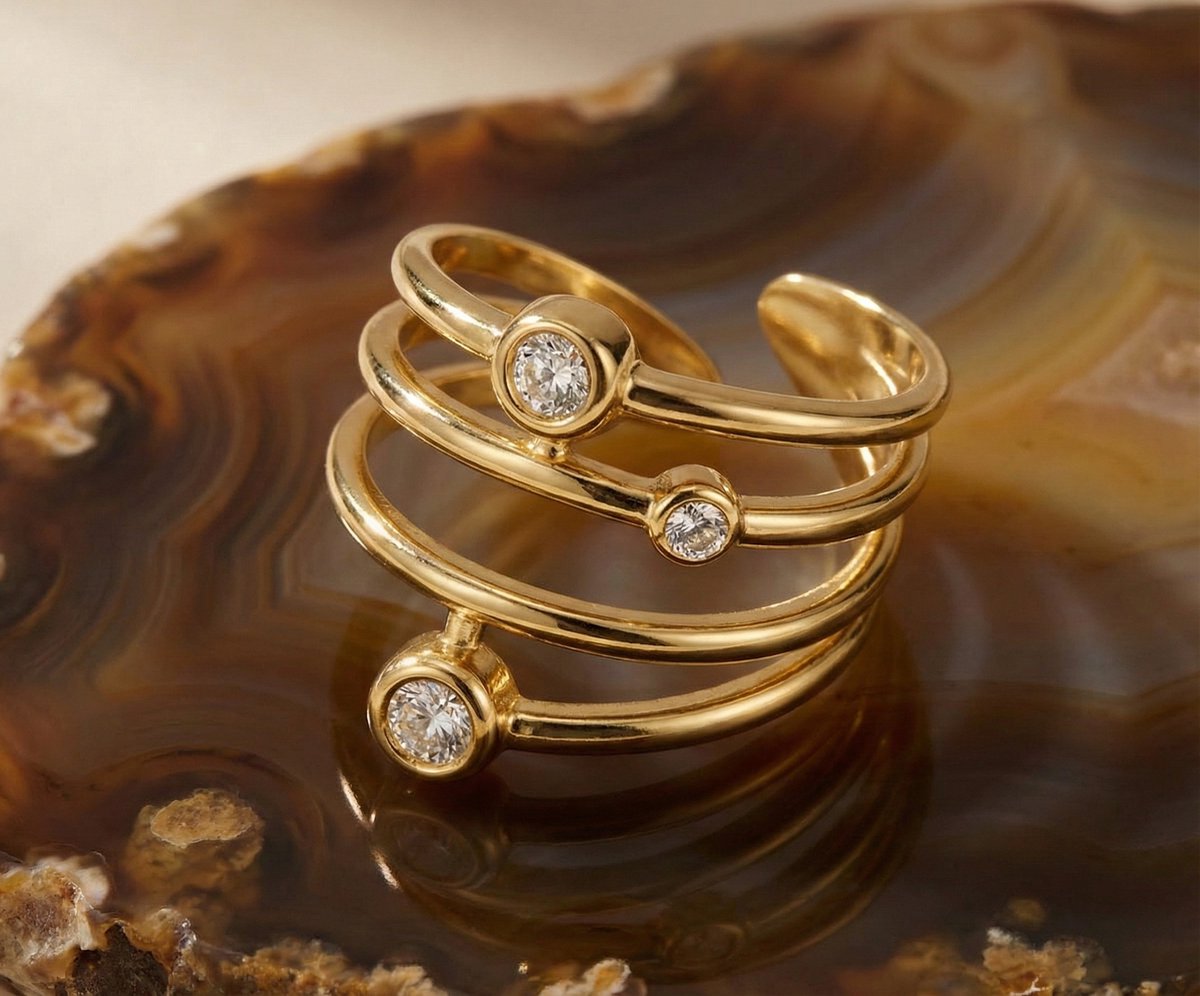 Lundholm Alexia goudkleurige verstelbare spiraal ring voor dames met drie fonkelende zirkonia steentjes, gefotografeerd op warme agaat natuursteen schaal voor sfeervolle productshot. Premium stainless steel met PVD gold plating van 2.5 micron, waterproof en hypoallergeen. Een verfijnd cadeau voor vrouw, moeder of vriendin op Moederdag of verjaardag in Scandinavisch design.