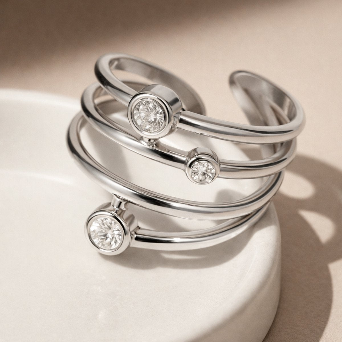 Lundholm Alexia zilverkleurige verstelbare spiraal ring voor dames met drie fonkelende zirkonia steentjes, gefotografeerd op crème keramische schaal voor elegante productshot. Premium stainless steel met PVD silver plating, waterproof en hypoallergeen. Een verfijnd cadeau voor vrouw, moeder of vriendin op Moederdag of verjaardag in Scandinavisch design.