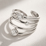 Lundholm Alexia zilverkleurige verstelbare spiraal ring voor dames met drie fonkelende zirkonia steentjes, gefotografeerd op witte gestructureerde stof voor stijlvolle productshot. Premium stainless steel met PVD silver plating, waterproof en hypoallergeen. Een verfijnd cadeau voor vrouw, moeder of vriendin op Moederdag of verjaardag in Scandinavisch design.