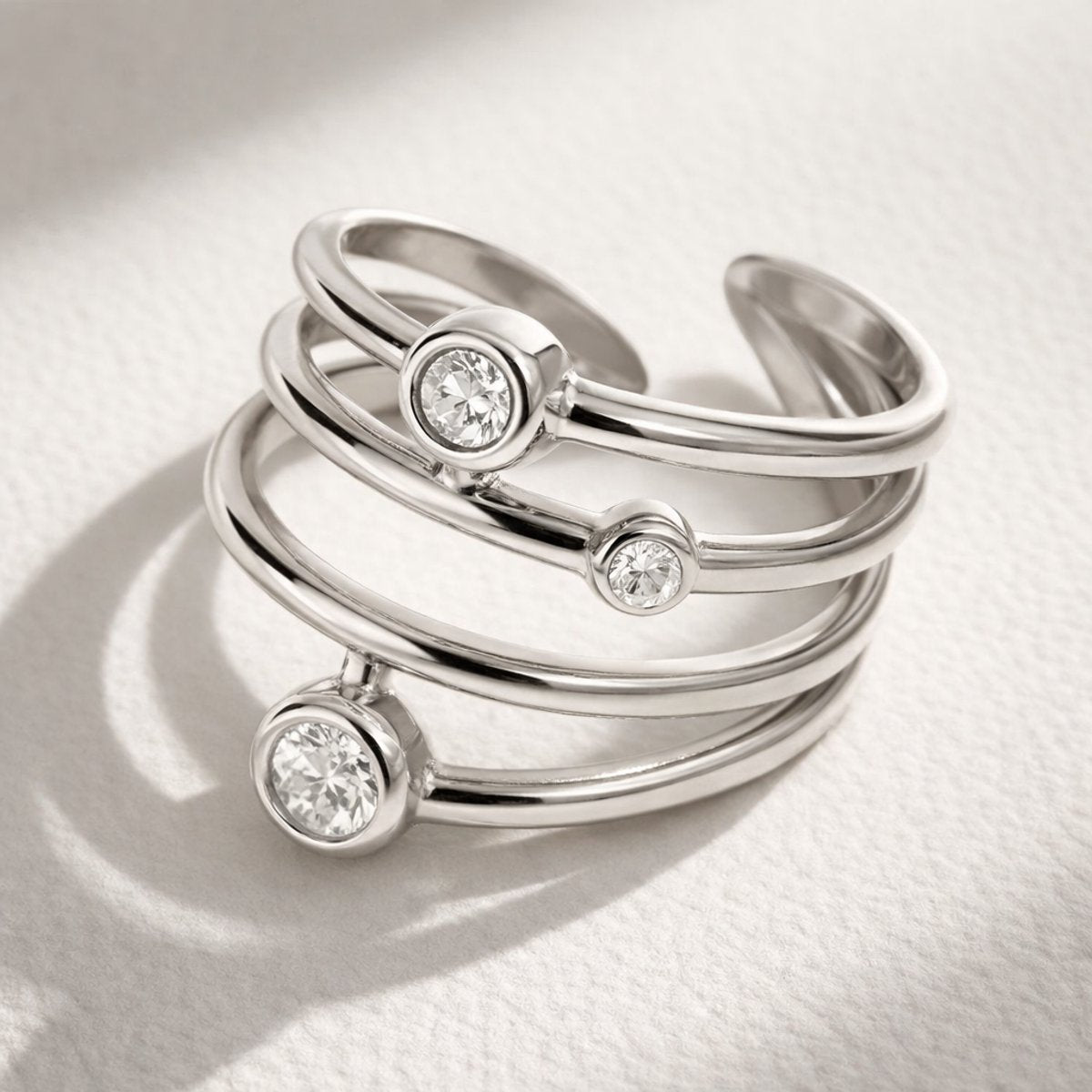 Lundholm Alexia zilverkleurige verstelbare spiraal ring voor dames met drie fonkelende zirkonia steentjes, gefotografeerd op witte gestructureerde stof voor stijlvolle productshot. Premium stainless steel met PVD silver plating, waterproof en hypoallergeen. Een verfijnd cadeau voor vrouw, moeder of vriendin op Moederdag of verjaardag in Scandinavisch design.