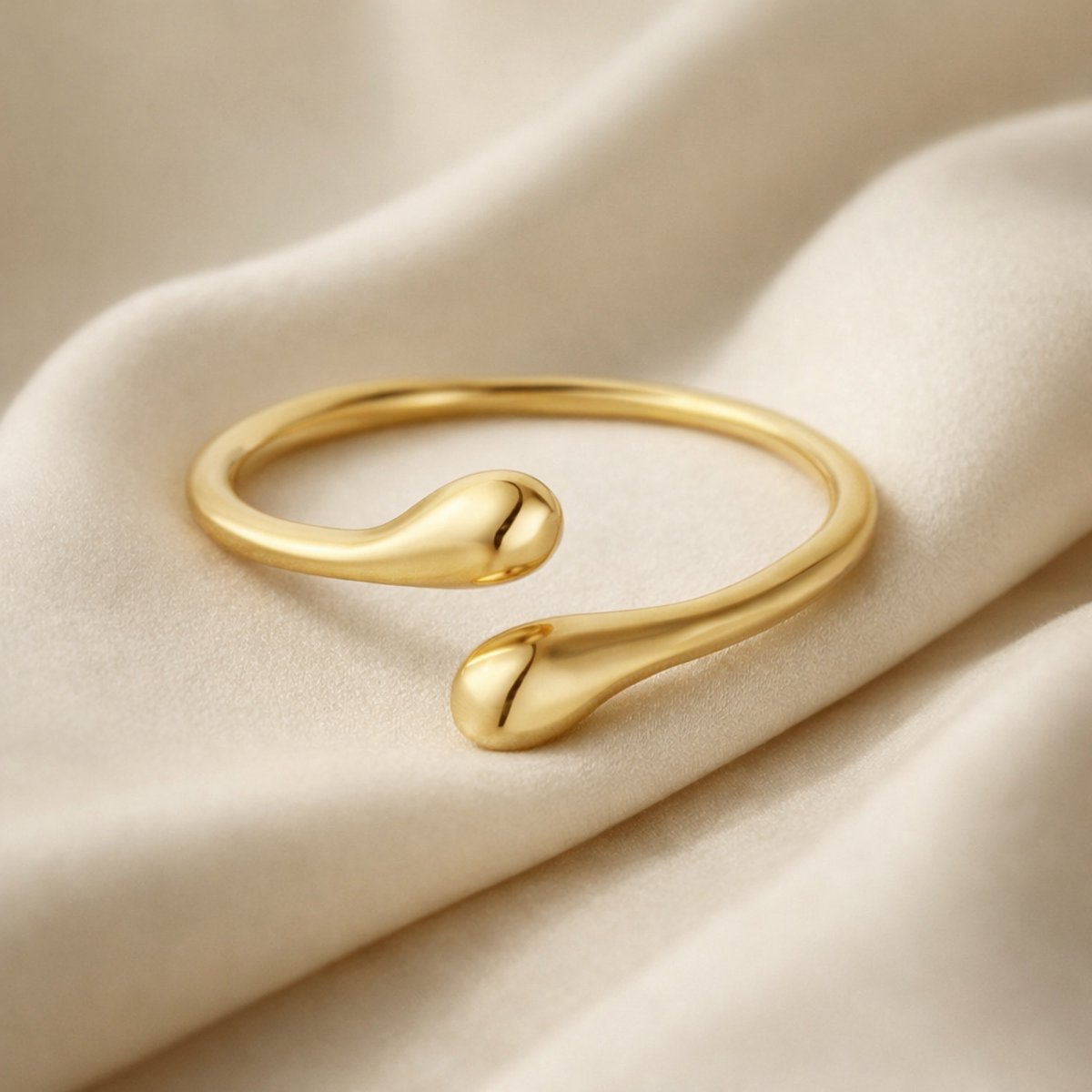 Lundholm Annabel goudkleurige verstelbare ring voor dames met minimalistisch open druppel uiteinden ontwerp, gefotografeerd op crème zijde voor elegante productshot. Premium stainless steel met PVD gold plating van 2.5 micron, waterproof en hypoallergeen. Een verfijnd cadeau voor vrouw, moeder of vriendin op Moederdag of verjaardag in Scandinavisch design.