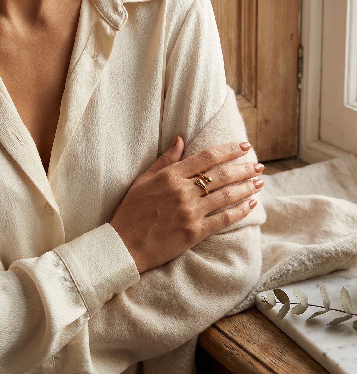Lundholm Annabel goudkleurige verstelbare ring voor dames met minimalistisch open druppel uiteinden ontwerp, gedragen door vrouw in crème blouse voor warme lookbook lifestyle shoot. Premium stainless steel met PVD gold plating van 2.5 micron, waterproof en hypoallergeen. Een verfijnd cadeau voor vrouw, moeder of vriendin op Moederdag of verjaardag in Scandinavisch design.