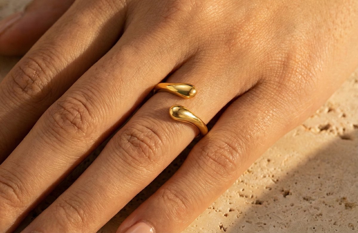 Lundholm Annabel goudkleurige verstelbare ring voor dames met minimalistisch open druppel uiteinden ontwerp, gedragen close-up op vinger met natuursteen achtergrond. Premium stainless steel met PVD gold plating van 2.5 micron, waterproof en hypoallergeen. Een verfijnd cadeau voor vrouw, moeder of vriendin op Moederdag of verjaardag in Scandinavisch design.