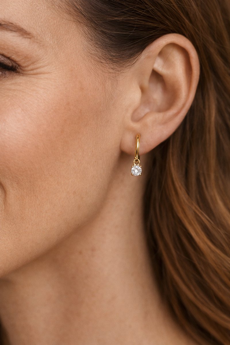 Lundholm Cathie goudkleurige huggie oorbel voor dames met fonkelende zirkonia steen hanger, gedragen door vrouw met rood haar voor close-up lookbook lifestyle shoot. Premium stainless steel met PVD gold plating van 2.5 micron, waterproof en hypoallergeen. Een elegant cadeau voor vrouw, moeder of vriendin op Moederdag of verjaardag in Scandinavisch design.