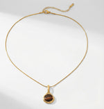 Lundholm Cecile Serie ketting voor dames in goudkleurig met natuurlijke tijgeroog hanger op witte achtergrond, gemaakt van premium stainless steel met PVD coating van 2.5 micron, waterproof en hypoallergeen, perfect cadeau voor vrouw, moederdag of verjaardag in Scandinavisch design.