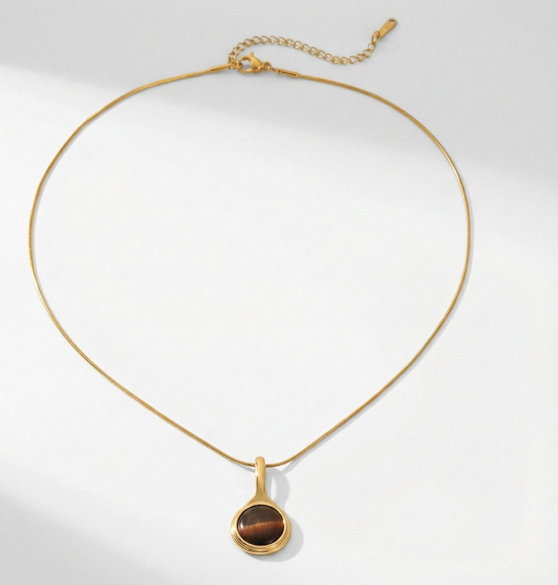 Lundholm Cecile Serie ketting voor dames in goudkleurig met natuurlijke tijgeroog hanger op witte achtergrond, gemaakt van premium stainless steel met PVD coating van 2.5 micron, waterproof en hypoallergeen, perfect cadeau voor vrouw, moederdag of verjaardag in Scandinavisch design.