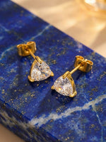 Lundholm Dani goudkleurige driehoek zirkonia oorknopjes dames op blauwe lapis lazuli edelsteen achtergrond - waterproof gold plated PVD premium stainless steel sieraden cadeau vrouw moederdag verjaardag Scandinavisch Design