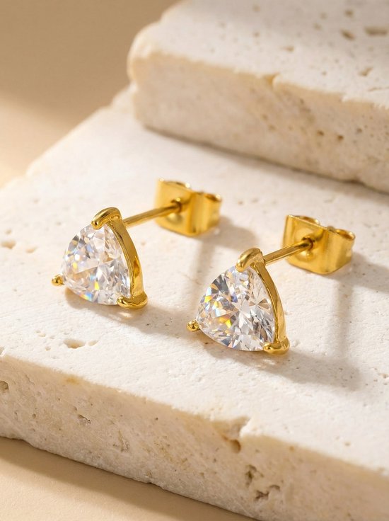 Lundholm Dani goudkleurige driehoek zirkonia oorknopjes dames op crème travertijn steen blok - waterproof gold plated PVD premium stainless steel sieraden cadeau vrouw moederdag verjaardag Scandinavisch Design