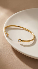 Lundholm Fem Serie open bangle cuff armband dames goudkleurig met zirkonia steentjes op crème keramische schaal lifestyle - waterproof gold plated PVD 2.5 micron premium stainless steel sieraden cadeau vrouw moederdag verjaardag Scandinavisch Design