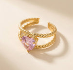 Lundholm Francine goudkleurige verstelbare statement ring voor dames met groot roze hart steen op getwist touw band, gefotografeerd op crème ondergrond voor stijlvolle productshot. Premium stainless steel met PVD gold plating van 2.5 micron, waterproof en hypoallergeen. Een romantisch cadeau voor vrouw, moeder of vriendin op Moederdag, Valentijnsdag of verjaardag in Scandinavisch design.