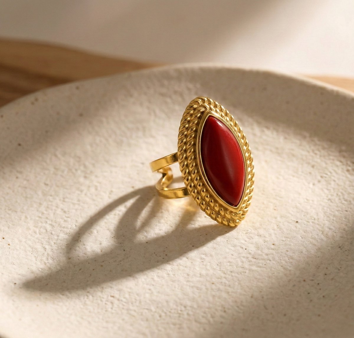 Lundholm Ivana goudkleurige verstelbare statement ring voor dames met grote rode marquise steen en touwpatroon detail in vintage ontwerp, gefotografeerd op crème keramische schaal voor warme productshot. Premium stainless steel met PVD gold plating van 2.5 micron, waterproof en hypoallergeen. Een opvallend cadeau voor vrouw, moeder of vriendin op Moederdag of verjaardag in Scandinavisch design.