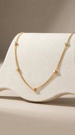 Lundholm minimalistische ketting dames goudkleurig verguld met mini hartjes 40cm op crème stof display productfoto - waterproof gold plated PVD premium stainless steel sieraden cadeau vrouw moederdag verjaardag Scandinavisch Design