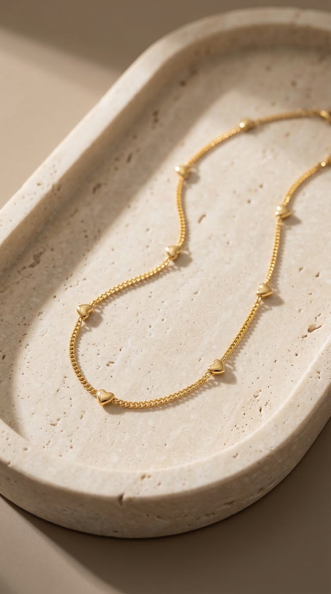 Lundholm minimalistische ketting dames goudkleurig verguld met mini hartjes 40cm op crème travertijn schaal productfoto - waterproof gold plated PVD premium stainless steel sieraden cadeau vrouw moederdag verjaardag Scandinavisch Design
