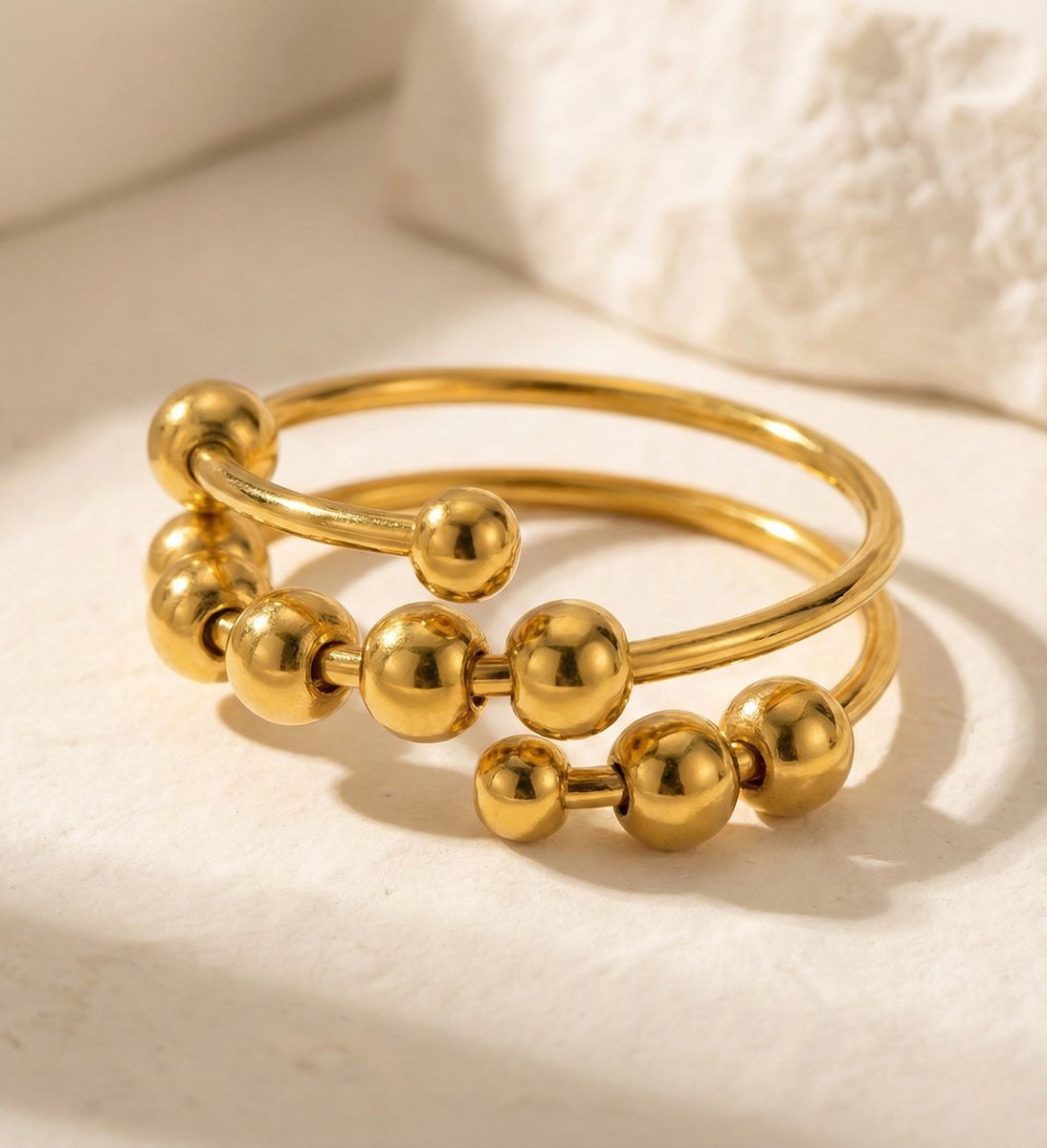 Lundholm Lauren goudkleurige verstelbare anxiety ring voor dames met schuifbare bolletjes en kralen voor stress relief en fidget, gefotografeerd op witte natuursteen voor stijlvolle productshot. Premium stainless steel met PVD gold plating van 2.5 micron, waterproof en hypoallergeen. Een doordacht cadeau voor vrouw, moeder of vriendin op Moederdag of verjaardag in Scandinavisch design.