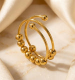 Lundholm Lauren goudkleurige verstelbare anxiety ring voor dames met schuifbare bolletjes en spiraal ontwerp voor stress relief en fidget, gefotografeerd op crème zijde voor luxe productshot. Premium stainless steel met PVD gold plating van 2.5 micron, waterproof en hypoallergeen. Een doordacht cadeau voor vrouw, moeder of vriendin op Moederdag of verjaardag in Scandinavisch design.