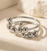 Lundholm Lauren zilverkleurige verstelbare anxiety ring voor dames met schuifbare bolletjes voor stress relief en fidget, gefotografeerd op witte natuursteen voor stijlvolle productshot. Premium stainless steel met PVD silver plating, waterproof en hypoallergeen. Een doordacht cadeau voor vrouw, moeder of vriendin op Moederdag of verjaardag in Scandinavisch design.