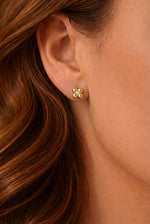 Lundholm Melle goudkleurige verfijnde oorknopjes voor dames met klein bloem ontwerp en zirkonia steen, gedragen door vrouw met rood haar voor close-up lookbook lifestyle shoot. Premium stainless steel met PVD gold plating van 2.5 micron, waterproof en hypoallergeen. Een subtiel cadeau voor vrouw, moeder of vriendin op Moederdag of verjaardag in Scandinavisch design.