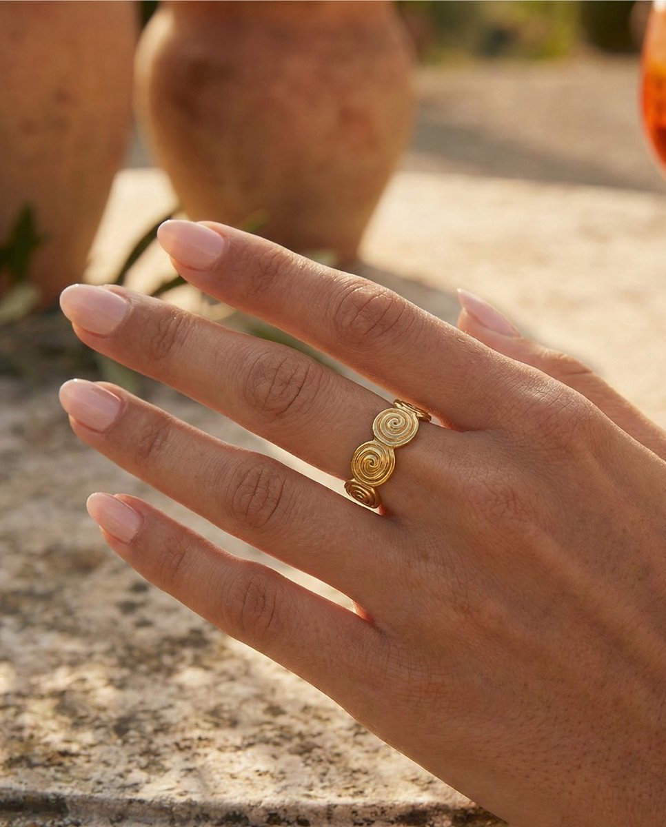 Lundholm Merel goudkleurige verstelbare ring voor dames met aesthetic spiraal swirl ontwerp, gedragen door vrouw met hand op natuursteen voor warme lookbook lifestyle shoot. Premium stainless steel met PVD gold plating van 2.5 micron, waterproof en hypoallergeen. Een unieke cadeau voor vrouw, moeder of vriendin op Moederdag of verjaardag in Scandinavisch design.