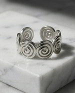 Lundholm Merel zilverkleurige verstelbare ring voor dames met aesthetic spiraal swirl ontwerp, gefotografeerd op witte marmeren ondergrond voor stijlvolle productshot. Premium stainless steel met PVD silver plating, waterproof en hypoallergeen. Een unieke cadeau voor vrouw, moeder of vriendin op Moederdag of verjaardag in Scandinavisch design.