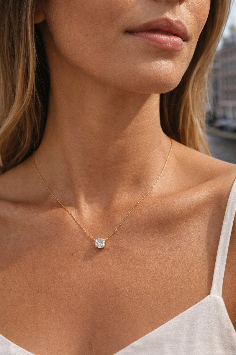 Lundholm Monique goudkleurige minimalistische ketting voor dames met fonkelende solitaire zirkonia steen hanger, gedragen door vrouw met witte top voor warme lookbook lifestyle shoot. Premium stainless steel met PVD gold plating van 2.5 micron, waterproof en hypoallergeen. Een tijdloos cadeau voor vrouw, moeder of vriendin op Moederdag of verjaardag in Scandinavisch design.