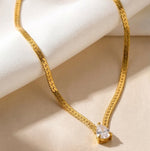 Lundholm My Ariane Serie luxe platte schakelketting dames goudkleurig verguld met druppel zirkonia steen hanger op crème stof productfoto - waterproof gold plated PVD premium stainless steel sieraden cadeau vrouw moederdag verjaardag Scandinavisch Design
