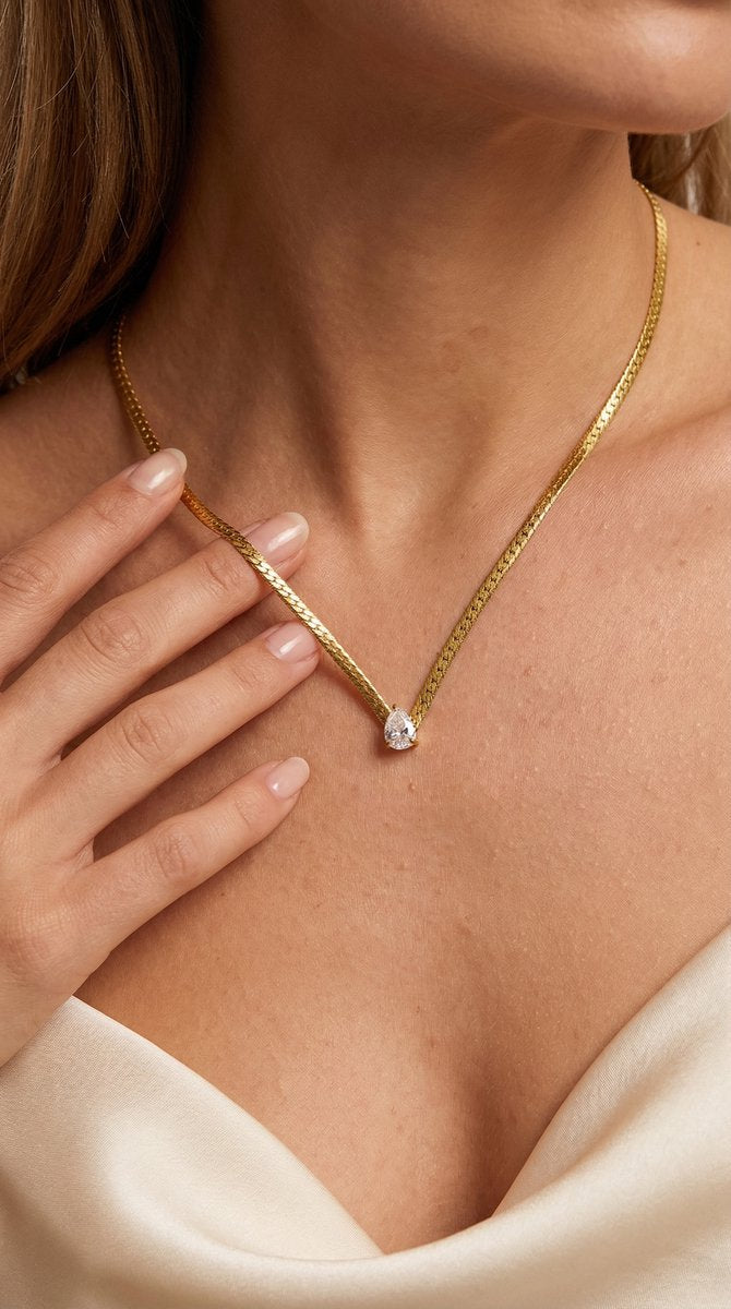 Lundholm My Ariane Serie luxe platte schakelketting dames goudkleurig verguld met druppel zirkonia hanger gedragen door model lifestyle decolleté - waterproof gold plated PVD premium stainless steel sieraden cadeau vrouw moederdag verjaardag Scandinavisch Design