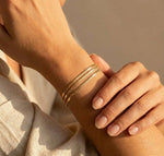 Lundholm My Bibi Serie luxe armband voor dames in goudkleurig met drie laags minimalistisch design gedragen aan pols van model in lifestyle setting, gemaakt van premium stainless steel met PVD coating van 2.5 micron, waterproof en hypoallergeen, perfect cadeau voor vrouw, moederdag of verjaardag in Scandinavisch design.