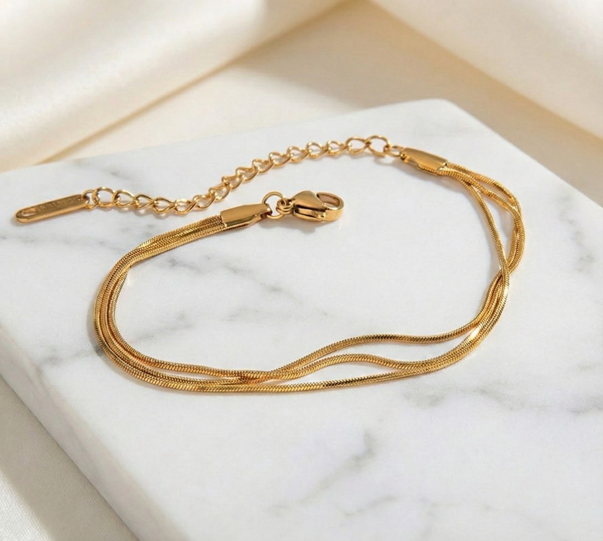 Lundholm My Bibi Serie luxe armband voor dames in goudkleurig met drie laags minimalistisch design, gemaakt van premium stainless steel met PVD coating van 2.5 micron, waterproof en hypoallergeen, gepresenteerd op marmer, perfect cadeau voor vrouw, moederdag of verjaardag in Scandinavisch design.