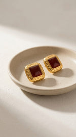 Lundholm My Felina Serie vintage stijl vierkante oorknopjes dames goudkleurig verguld met bordeaux rode steen op crème keramische schaal lifestyle - waterproof gold plated PVD premium stainless steel sieraden cadeau vrouw moederdag verjaardag Scandinavisch Design