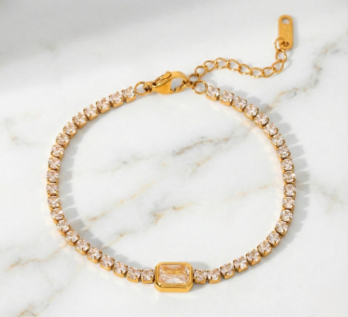 Lundholm My Jasmijn Serie luxe armband voor dames in goudkleurig met zirkonia stenen in tennis-stijl met centrale rechthoekige zirkonia op marmeren ondergrond, gemaakt van premium stainless steel met PVD coating van 2.5 micron, waterproof en hypoallergeen, perfect cadeau voor vrouw, moederdag of verjaardag in Scandinavisch design.