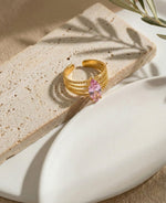 Lundholm My Juliette goudkleurige verstelbare cuff ring voor dames met grote roze marquise natuursteen in vintage ontwerp, gefotografeerd op travertijn met olijfblad voor warme mediterrane productshot. Premium stainless steel met PVD gold plating van 2.5 micron, waterproof en hypoallergeen. Een romantisch cadeau voor vrouw, moeder of vriendin op Moederdag of verjaardag in Scandinavisch design.