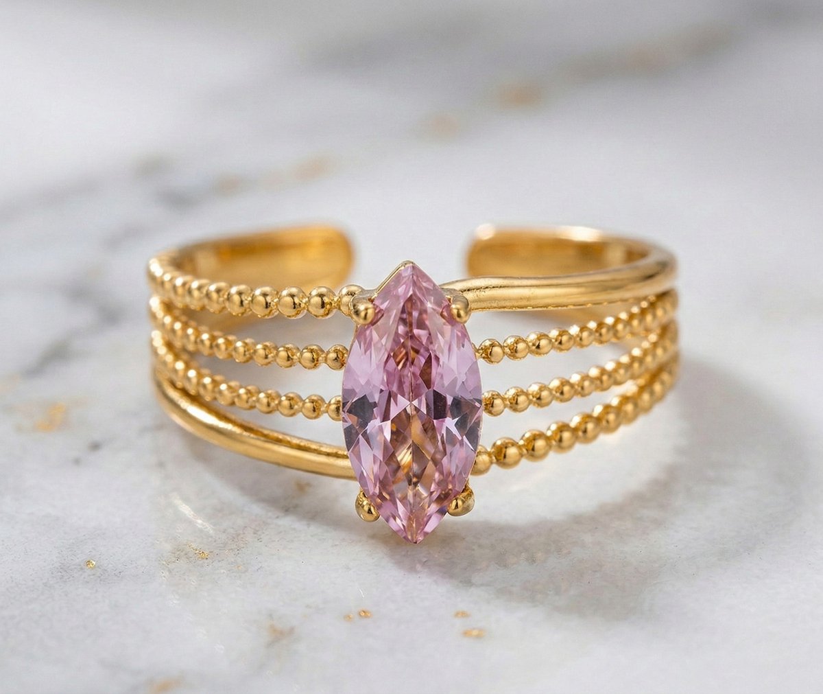 Lundholm My Juliette goudkleurige verstelbare cuff ring voor dames met grote roze marquise natuursteen op gestippelde band, gefotografeerd op witte marmeren ondergrond voor luxe productshot. Premium stainless steel met PVD gold plating van 2.5 micron, waterproof en hypoallergeen. Een romantisch cadeau voor vrouw, moeder of vriendin op Moederdag of verjaardag in Scandinavisch design.