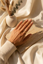Lundholm My Linda goudkleurige verstelbare ring voor dames met minimalistisch geometrisch golf ontwerp, gedragen door vrouw met hand op travertijn steen naast vaas met droogbloemen voor lookbook lifestyle shoot. Premium stainless steel met PVD gold plating van 2.5 micron, waterproof en hypoallergeen. Een tijdloos cadeau voor vrouw, moeder of vriendin op Moederdag of verjaardag in Scandinavisch design.