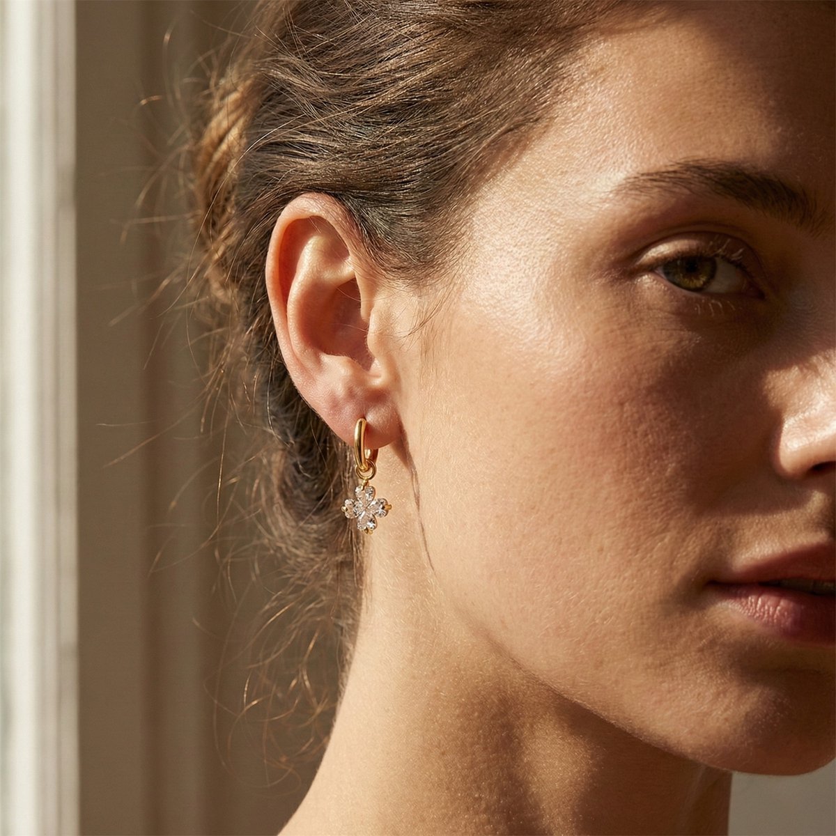 Lundholm My Lycka goudkleurige geluksoorbellen voor dames met klavertje vier hanger ingelegd met fonkelende zirkonia, gedragen door vrouw voor close-up lookbook lifestyle shoot. Premium stainless steel met PVD gold plating van 2.5 micron, waterproof en hypoallergeen. Een betekenisvol cadeau voor vrouw, moeder of vriendin op Moederdag of verjaardag in Scandinavisch design.